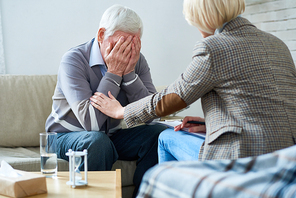 Portrait of depressed senior man crying during therapy session with female psychiatrist trying to console him