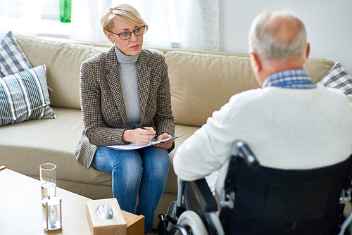 Portrait of mature female psychiatrist interviewing handicapped senior man during therapy session, copy space