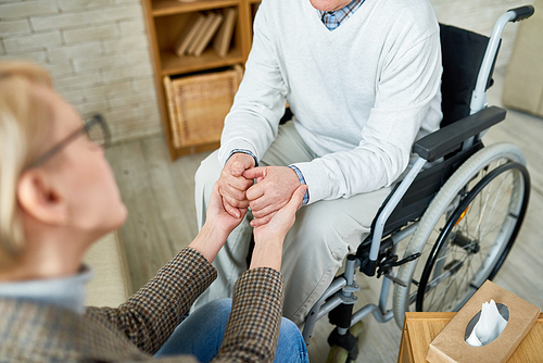 High angle close up of female therapist holding hands with senior patient in wheelchair, comforting him in difficult situation, copy space