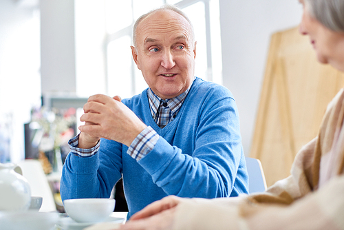 Portrait of nice senior couple enjoying conversation while drinking tea at home, focus on balding elderly man talking to wife, copy space