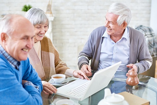 Portrait of three modern senior people using laptop in retirement home and smiling happily, copy space