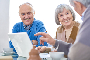 Cheerful elderly patients in assisted living home sharing laptop while chilling at table and drinking tea.