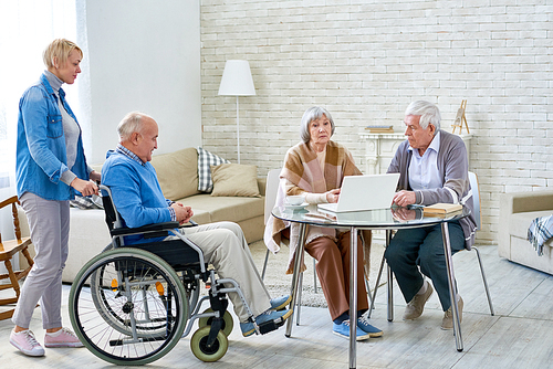 Full length portrait of several senior people enjoying free time in retirement home, one of them in wheelchair, copy space