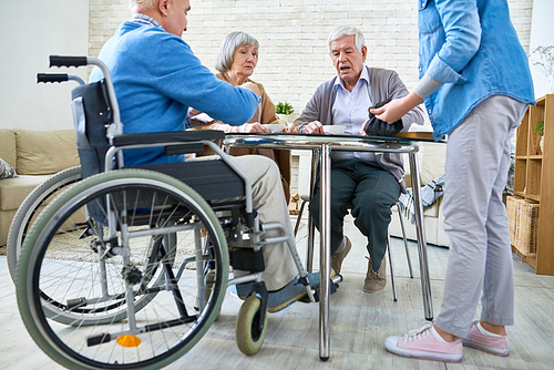 Full length portrait of group of senior people playing board games sitting round table in retirement home, copy space