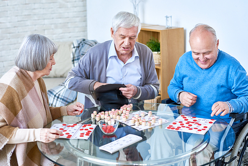 Portrait of senior people playing lotto game sitting at glass table in living room of retirement home