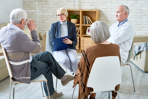 Portrait of blonde female psychiatrist leading group therapy session for senior people in retirement home, copy space, copy space