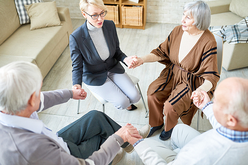 High angle view at senior people holding hands in group therapy session lead by female psychiatrist, copy space