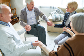 Portrait of senior people holding hands in group therapy session lead by female psychiatrist, copy space