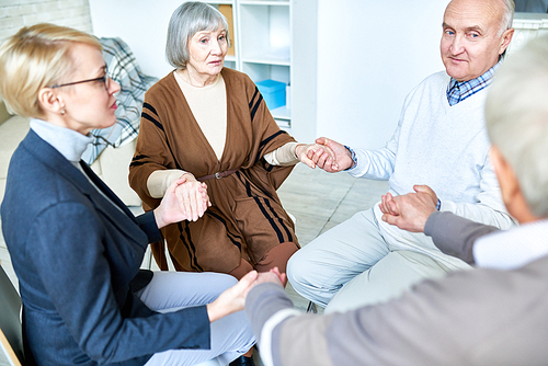 Elderly patients sitting in circle with therapist and holding hands on consultation in assisted living home.