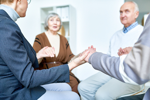 Group of senior people holding hands in group therapy session lead by female psychiatrist, copy space
