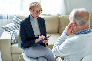 Portrait of blonde female psychologist talking to senior man during consultation, copy space