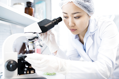 Portrait of Asian female scientist looking in microscope while doing research in medical laboratory