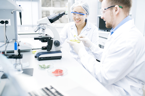 Portrait of two modern young scientists smiling while doing research studying food substances in laboratory, copy space