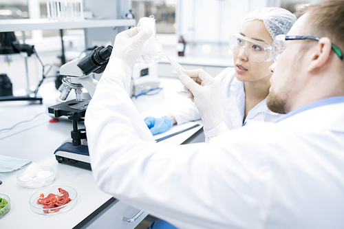 Portrait of two modern scientists, man and woman,  taking probe for medical research studying liquids in beaker while sitting at table in laboratory