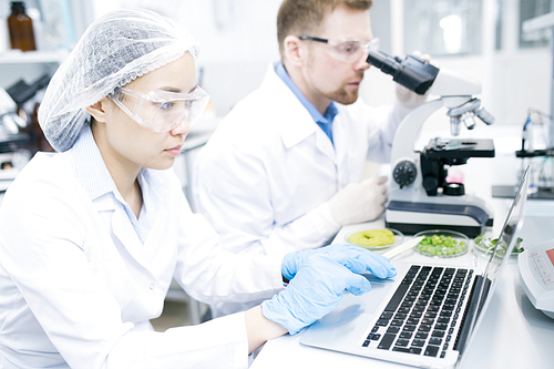 Portrait of two modern young scientists doing research studying substances in laboratory and using laptop, copy space