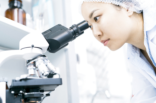 Portrait of young Asian woman  looking in microscope while doing research in medical laboratory