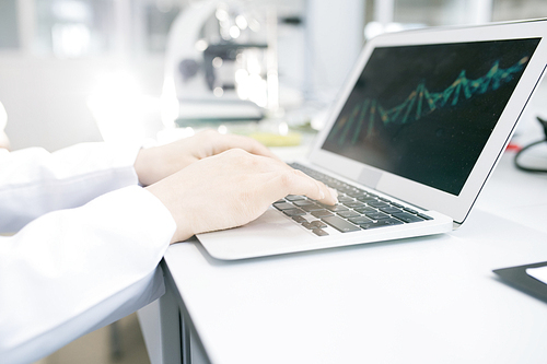 Crop view of hands of microbiologist working on food nutrition problem analyzing DNA model of green vegetable test object on laptop