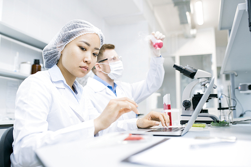 Portrait of two modern scientists studying substances while working on research in medical laboratory, focus on young Asian woman in front