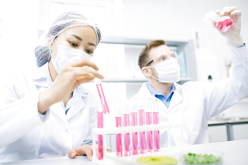 Crop view of scientists sitting with test tubes and flask with pink liquid conducting laboratory experiments with meat