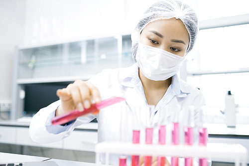 Portrait of Asian female scientist working on research studying liquids in beakers while sitting at table in laboratory