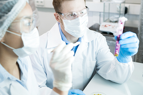 Portrait of two modern scientists working on medical research studying liquids in beaker while sitting at table in laboratory