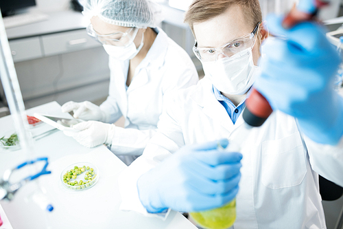 High angle portrait of two modern scientists working on medical research studying liquids in beaker while sitting at table in laboratory