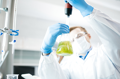 Crop view of microbiologist surveying sample of green vegetable solution studying it nutrition in laboratory