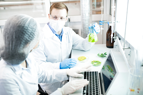 Portrait of two modern scientists working on food research studying liquids in beaker while sitting at table in laboratory