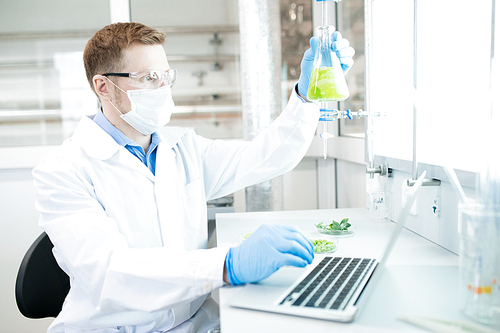 Side view  portrait of modern scientists working on medical research studying liquids in beaker while sitting at table in laboratory