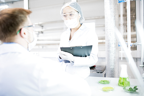 Portrait of two modern young scientists wearing lab coats talking while working in medical laboratory