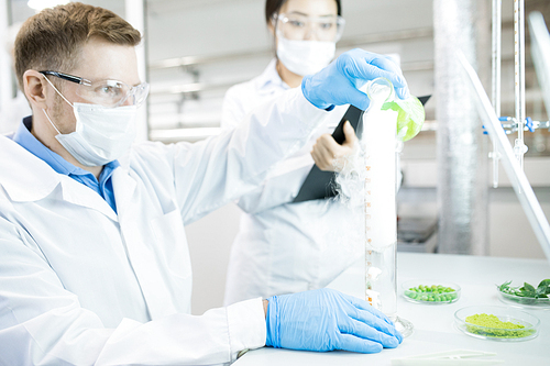 Portrait of two scientists working on food research studying liquids in beaker while sitting at table in laboratory