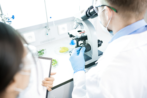 High angle portrait of two scientists working on research and using microscope while sitting at table in laboratory