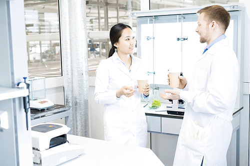 Waist up portrait of two modern young scientists wearing lab coats  chatting while taking break from working in medical laboratory