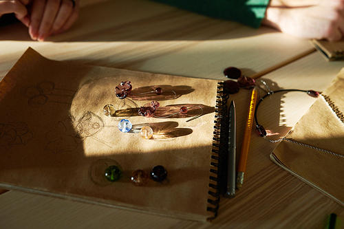 Background image of colorful glass beads in sunlight lying on table with jewelry sketches at creative workshop, copy space