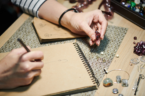 Closeup of unrecognizable woman drawing sketches while creating beautiful handmade jewelry, copy space