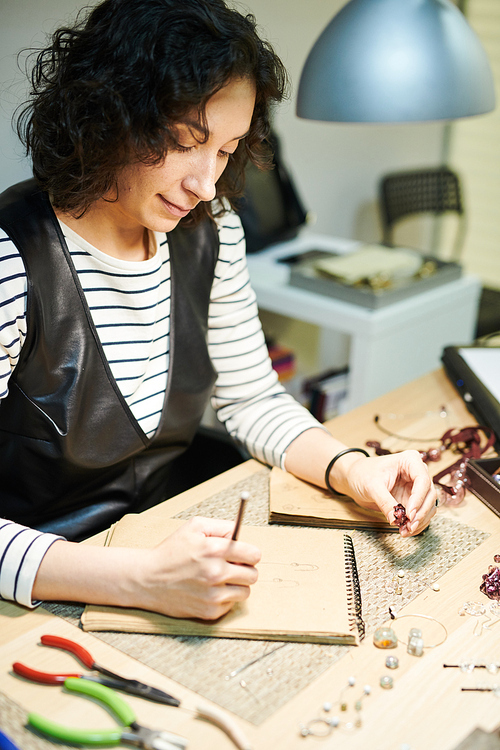 Portrait of female artist drawing sketches while creating beautiful handmade jewelry, copy space