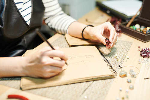 Close up of unrecognizable woman drawing sketches while creating beautiful handmade jewelry, copy space