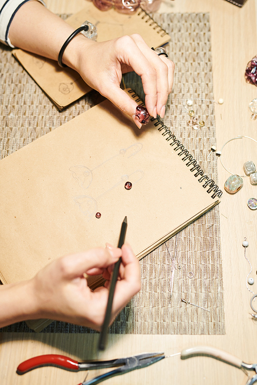 Above view close up of unrecognizable woman drawing sketches while creating beautiful handmade jewelry, copy space
