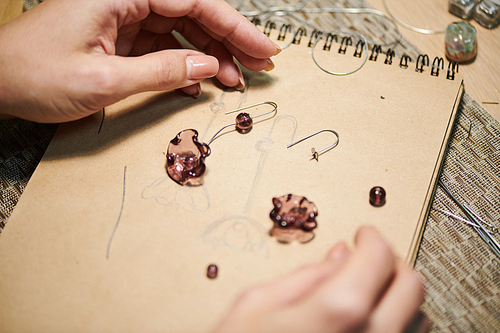Close up of female hands drawing sketches while creating beautiful handmade jewelry, copy space