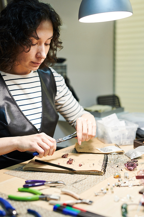 Portrait of young woman creating beautiful handmade jewelry in workshop, copy space