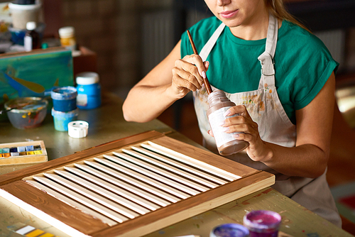Mid-section portrait of young female artist enjoying work in art studio painting shutters with bronze paint, making DIY interior decoration