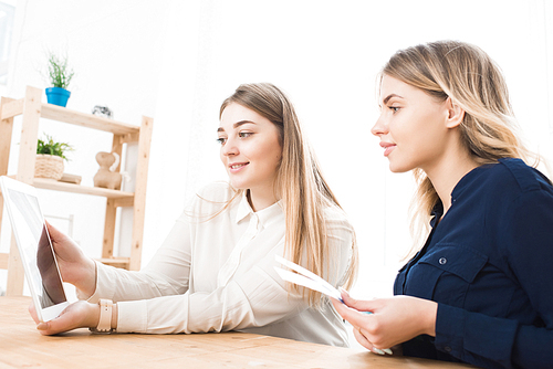 Two young women sitting at the table and looking something on digital tablet