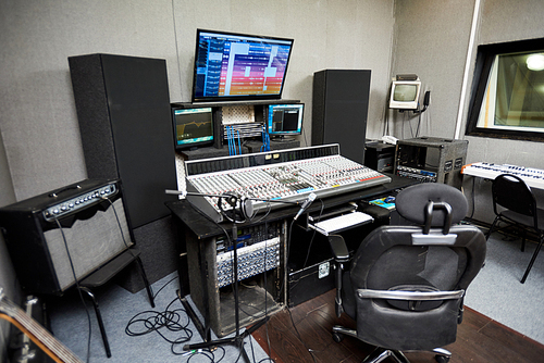 Modern audio workstation equipped with computer, microphone on stand, control surface and loudspeakers
