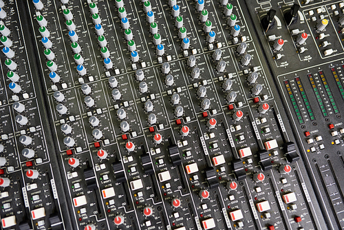 Background image of refined fader knobs and SSL channels on black recording board in music studio
