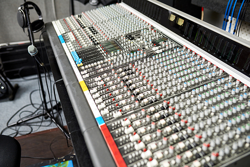 Mixing desk used for combining sounds of many different audio signals and microphone on stand with headphones in studio