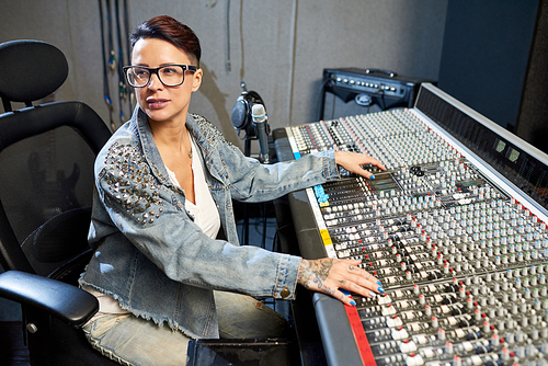Stylish woman working with control console in music recording studio looking away in process.