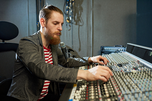 Concentrated man working with music board in modern sound recording studio.