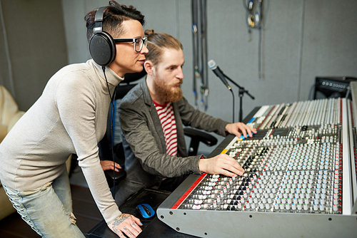 Man and woman working together on music creation standing at electronic board in sound studio.