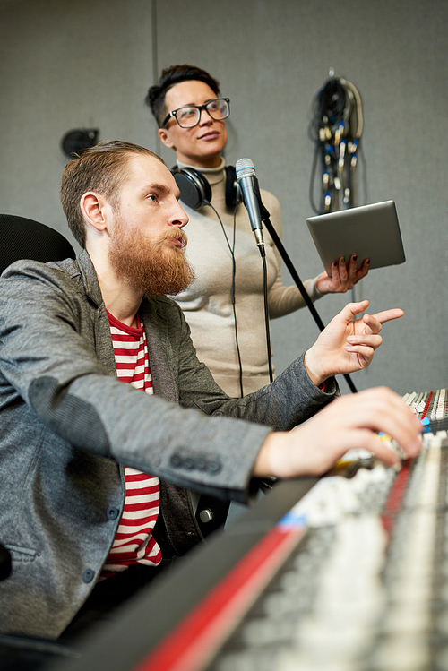 Side view of confident man and woman discussing ideas while composing music in recording studio.
