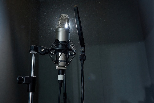 From below shot of professional recording microphone against bright spotlight in sound studio.